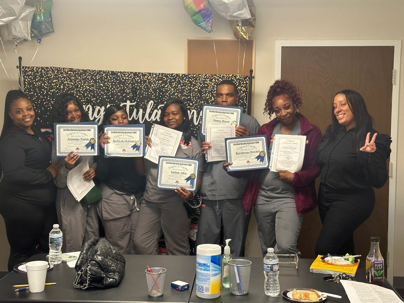A cohort of students in scrubs holding certificates under a congratulations backdrop
