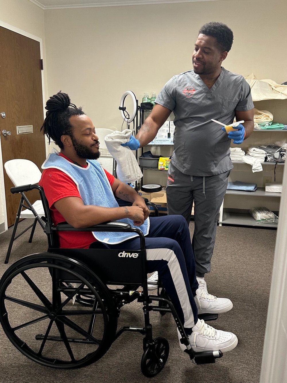 A student assisting a person in a wheelchair in a clinical room